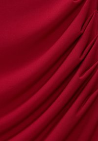 Tissu rouge profond avec une texture lisse et de doux plis rassemblés d'un côté.