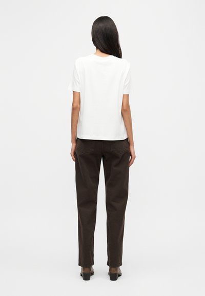Λευκό βαμβακερό t-shirt με κοντά μανίκια, σε συνδυασμό με σκούρο καφέ παντελόνι. Λείο ύφασμα, χαλαρή εφαρμογή και μινιμαλιστικός σχεδιασμός.
