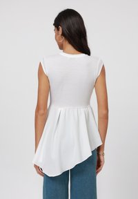 Valge peplum top, mis on valmistatud kergest kangast, ümmarguse kaeluse, lühikeste varrukate ja voogava, asümmeetrilise lõhikuga.