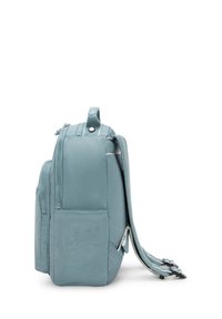 Zaino compatto blu chiaro con tasche frontali e laterali con zip, spallacci imbottiti e maniglia superiore, mostrato di lato su uno sfondo bianco.
