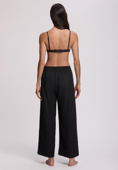 Μαύρο σουτιέν bralette με ρυθμιζόμενους ιμάντες και κλείσιμο με αγκράφα, σε συνδυασμό με μαύρο, φαρδύ παντελόνι με ελαστική μέση και φαρδιές γραμμές.