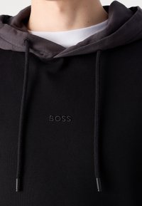 Sudadera negra con forro gris, con cordones ajustables y un logotipo bordado de "BOSS". Textura suave con un ajuste cómodo.