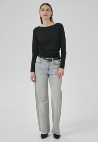 Svart långärmad topp med båthals, tillsammans med ljusblå högmidjade vida jeans och svarta spetsiga klackskor.