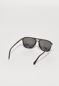 Ochelari de soare cu o ramă rectangulară, din material plastic negru, lentile polarizate gri, brațe subțiri și accente metalice aproape de balamale.