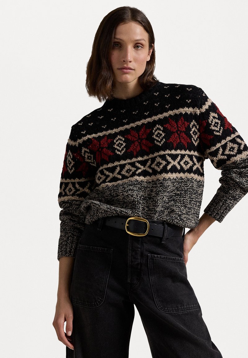 Pulover negru din tricot cu modele geometrice roșii și bej, guler rotund și mâneci lungi. Asortat cu blugi închiși la culoare cu talie înaltă și o curea cu cataramă aurie.