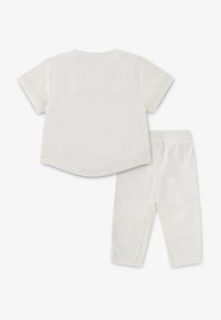 Hvid strikket kortærmet skjorte med afrundet kant og matchende leggings. Begge dele har en blød tekstur og elastisk taljebånd.