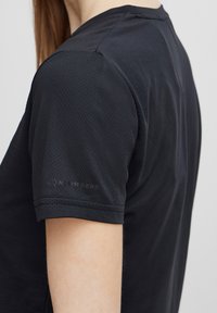 Must  lühikeste varrukatega treeningpaita tekstureeritud kangast. Omab õlavarre peent logo ja ümmargust krae disaini.