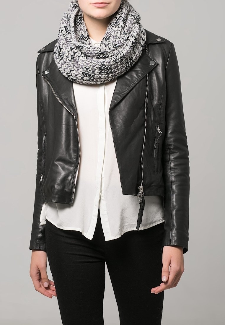 Personne portant une veste en cuir noire, une chemise blanche, un pantalon noir et une grosse écharpe tricotée gris et blanc sur fond gris.