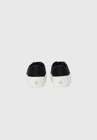 Black corduroy sneakers with white rubber soles, featuring a textured upper and a logo detail on the heel. Designed for casual wear.