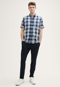 Kurzärmliges karierte Hemd in Marineblau und Hellblau mit Knopfleiste, kombiniert mit dunklen Hosen und weißen Sneakern.