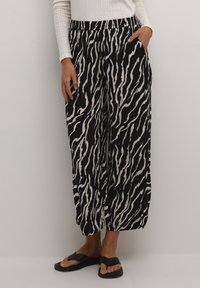 Black and cream wide-leg pants with a zebra print design, featuring an elastic waistband and side pockets. Worn with black sandals.
