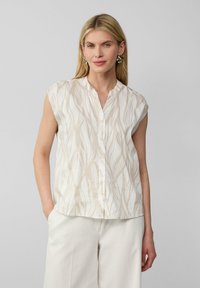 Ärmellose Bluse in Creme mit beigen abstrakten Blattmustern, mit Knopfleiste und Stehkragen. Glattes Material, lockere Passform.