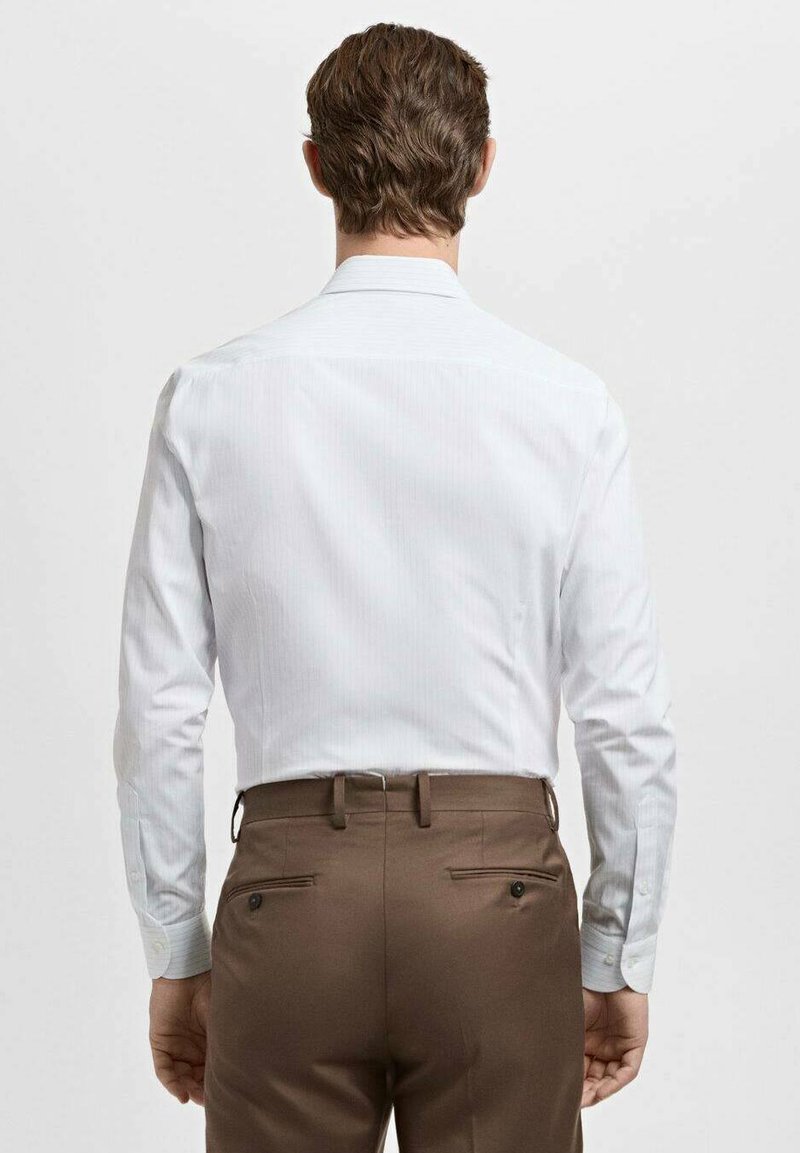 Chemise blanche à rayures avec manches longues, dotée d'un col classique. Associée à un pantalon marron ajusté avec des poches arrière décoratives.