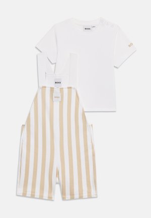Maglietta bianca a maniche corte con logo "BOSS" beige e salopette a righe verticali beige e bianche con cerniera frontale e spalline.