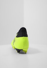 Fotbalová kopačka s jasně neonově žlutým síťovaným svrškem a černými akcenty, texturovaným povrchem a tvarovanými kolíky pro trakci.