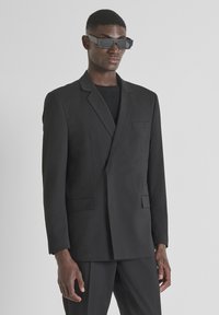 Crni odijelo s dodatkom s dva prednja džepa, zatvaranjem na jedan gumb i reverima u obliku ušice. Teksturirana tkanina u klasičnom kroju.