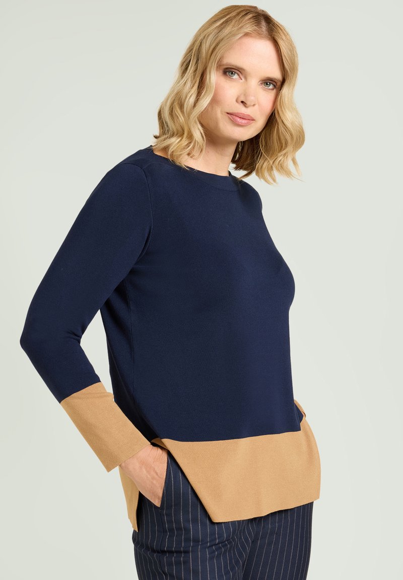 Top de manga larga azul marino con dobladillo inferior y mangas en marrón claro. Presenta un escote redondo y aberturas laterales en la base.