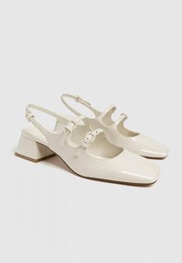 Chaussures à talons bas en cuir synthétique blanc cassé pour femmes, à lanières et avec bouts carrés arrondis, ornées de doubles boucles sur le dessus.