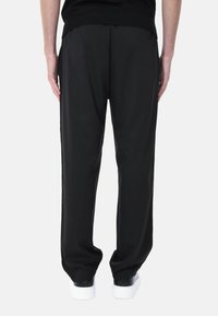 Pantaloni neri realizzati in tessuto morbido con una vestibilità ampia, caratterizzati da un design a gamba dritta e una vita elasticizzata. Sneakers bianche visibili sotto.