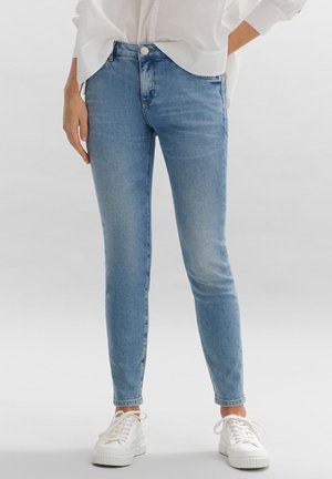 Lichtblauwe denim skinny jeans met een hoge taille, voorzien van een klassiek vijf-pocket ontwerp en een metalen knoopsluiting, gecombineerd met witte sneakers.