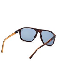 Occhiali da sole tartaruga con lenti blu, caratterizzati da una montatura robusta, un design elegante e un accento arancione sulle tempie.