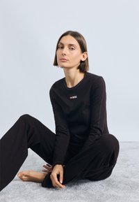 Camisola de manga longa preta e calças combinando em tecido macio. A camisola apresenta um pequeno logotipo vermelho "DIESEL" no peito. Ajuste simples e relaxado.