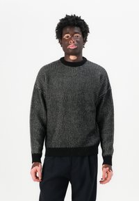 Maglione chunky di colore nero con macchie bianche, polsini e orlo a coste, scollatura rotonda e design morbido.