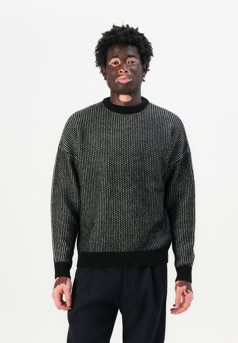 Dicker Strickpullover in Schwarz mit weißen Sprenkeln, gerippten Bündchen und Saum, runder Ausschnitt und lockerer Passform.