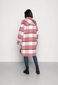 Rutig oversized kappa i rosa, vitt och brunt. Mjuk tyg med krage, långa ärmar och sidofickor. Bärs med blåjeans och svarta stövlar.