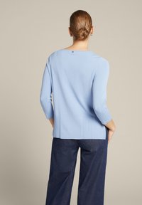 Helles, blaues langärmliges Sweatshirt mit gerippter Textur an den Seiten und am Rücken, mit einem Bootsausschnitt und einem leicht längeren Saum auf der Rückseite.