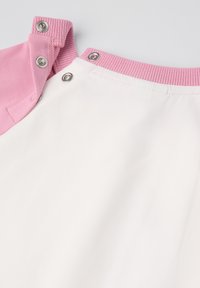 Korte mouw top met een roze kraag en een witte body. Heeft drukknoopsluitingen op de schouder. Gemaakt van zachte, gladde stof met een matte afwerking.