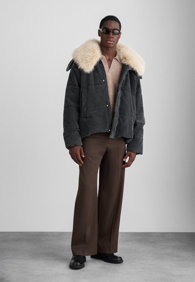 Γκρι σακάκι από κορδόνι με γιακά από συνθετική γούνα, συνδυασμένο με μπεζ πουλόβερ και καφέ παντελόνι φαρδύ, με σκούρα παπούτσια.