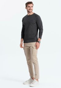 Dunkelgraues Langarmshirt mit einer Brusttasche, kombiniert mit beigen Cargo-Hosen mit seitlichen Taschen und weißen Sneakers.