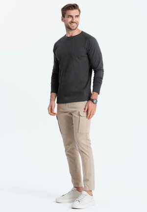 Dunkelgraues Langarmshirt mit einer Brusttasche, kombiniert mit beigen Cargo-Hosen mit seitlichen Taschen und weißen Sneakers.
