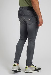 Jeans de mezclilla gris ajustados con un acabado texturizado, que cuentan con dos bolsillos traseros y una etiqueta de marca en la cinturilla. Combinados con zapatillas multicolores.