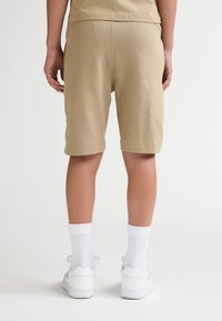 Beige bomuldsshorts med elastisk talje, der ender lige over knæet, kombineret med hvide ankelsokker og hvide sneakers. Set bagfra.