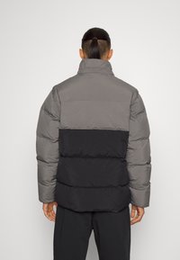 Puffjacka med en grå övre del och svart nedre del. Har en hög krage, quiltad textur och en avslappnad passform. Enkelt design.