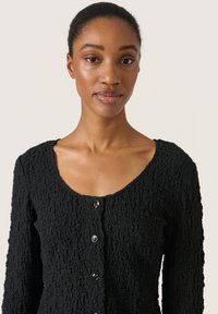 Cardigan nero con texture, girocollo, maniche lunghe e cinque bottoni neri sul davanti. Presenta un design di tessuto sgualcito.