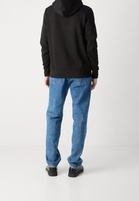 Felpa nera con tasca a marsupio, abbinata a jeans in denim blu con una vestibilità comoda e tasche posteriori classiche. Scarpe nere completano il look.