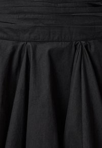 Zwarte stoffen rok met horizontale plooien bij de taille en zachte, vloeiende plooien hieronder. Het materiaal heeft een zachte textuur.