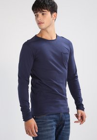 Navy long-sleeve t-shirt made of cotton, featuring a round neckline and a chest pocket. Soft texture and fitted design.