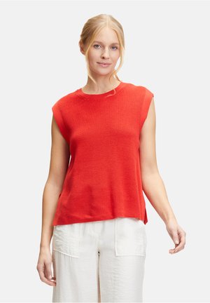 Red sleeveless knit top with a textured pattern, round neckline, and side slits, paired with white linen pants featuring large pockets.