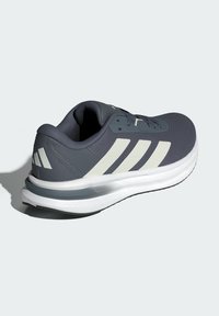 Gray athletic shoe with textured upper, white accents, and three stripes design. Features cushioned sole labeled "CLOUDFOAM."