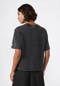 Czarna bawełniana koszulka z luźnym krojem, krótkimi rękawami i okrągłym dekoltem. Posiada wyblakłe wykończenie oraz małe logo na lewym rękawie.