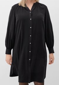 Robe noire à boutonnage, avec une coupe décontractée, en tissu doux, à manches longues en forme de ballon, col mandarin et fentes sur les côtés.