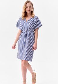 Pasiasta sukienka w niebiesko-białe paski, z dekoltem w serek, krótkimi szerokimi rękawami oraz ściągniętym w talii sznurkiem. Gładka struktura tkaniny.