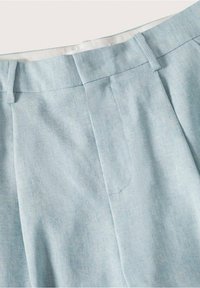 Pantalon en lin bleu clair à la texture lisse, doté d'un devant plat, d'une ceinture, et d'une seule poche sur le côté gauche.