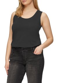 Zwarte mouwloze top met een ronde hals, gemaakt van een gladde stof, gecombineerd met donkergrijze jeans met een vo zak.