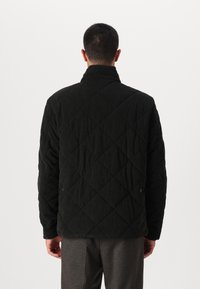 Μαύρο καπιτονέ μπουφάν με διαμαντένιο μοτίβο, ψηλό γιακά, μακριά μανίκια και υφασμάτινη υφή. Διαθέτει κουμπιά με πίεση στα πλάγια.