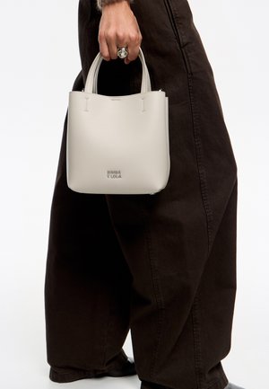 Bolso de mano de cuero gris claro con un diseño estructurado, que presenta dos asas cortas, un cierre de cremallera y un logo en relieve en la parte inferior.